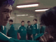 a man with purple hair is holding another man 's hand in a room with other people .