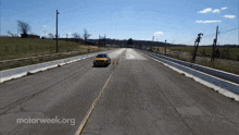 a yellow car is driving down a road next to a motorweek.org sign