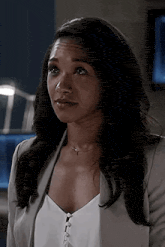 a woman in a white top and gray jacket is standing in a room .