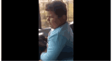 a young boy in a blue shirt is looking out of a bus window .