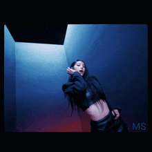 a woman in a black crop top is standing in a dark room with the word ms on the bottom right