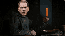 a man in a black jacket holds a carrot in his hand