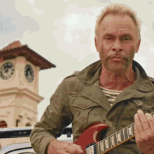a man playing a guitar in front of a large clock tower