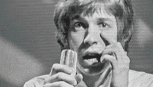 a black and white photo of a man holding a microphone in his hand and blowing his nose .