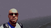 a bald man wearing sunglasses stands next to a man in a brown jacket