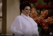 a woman wearing a white robe is standing in front of flowers .