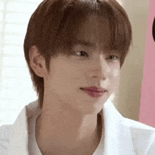 a close up of a young man with brown hair wearing a white shirt and looking at the camera .