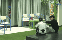 a man kneeling next to a woman in a room with a gma sign behind them
