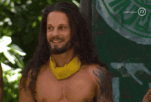 a shirtless man with long hair and a yellow scarf around his neck is smiling in front of a green background that says premijera