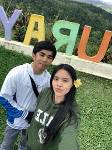 a man and a woman are posing for a picture in front of a sign that says yaju