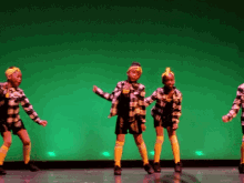 a group of kids are dancing on a stage with a green background