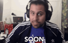a man wearing headphones and a blue shirt with the word soon on it