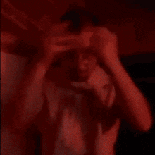 a man in a white shirt and tie is sitting in a dark room with a red light behind him .