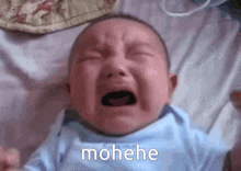 a baby in a blue shirt is crying with the word mohehe written below it