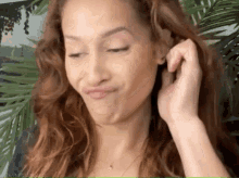 a woman with curly hair is making a funny face while touching her ear .