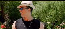 a man wearing a hat and sunglasses is standing in front of a tree .