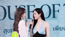 two women are standing next to each other and talking into microphones in front of a sign .
