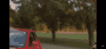 a red car is parked on the side of the road in front of trees