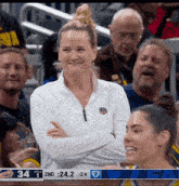 a woman stands in the stands with her arms crossed in front of a scoreboard that says 34 on it