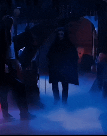 a group of people are standing in a dark room with a blue light behind them