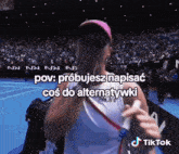 a woman in a pink hat is covering her face with her hand in front of a crowd and a tiktok logo
