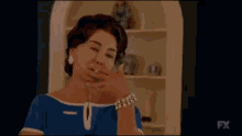 a woman in a blue dress is holding her hand to her mouth .