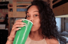 a woman drinking from a green cup with the word boohoo on the back