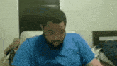 a man in a blue shirt is sitting in a chair making a funny face