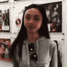 a woman wearing a hoodie and sunglasses is standing in front of a wall with pictures on it .