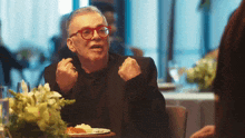 a man with red glasses is sitting at a table with a plate of food on it