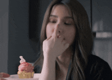 a woman is eating a cupcake with a strawberry frosting