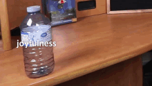 a bottle of water sits on a wooden table with joyfulness written above it