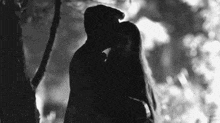 a man and a woman are kissing under a tree at night .