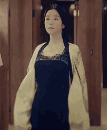 a woman in a black dress and a white jacket is standing in a dressing room .