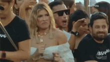 a woman is standing in a crowd of people wearing sunglasses and making a funny face .