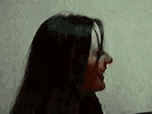 a close up of a woman 's face with long black hair against a wall .