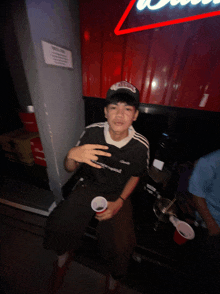 a man sitting under a budweiser sign holding a cup