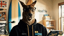 a kangaroo wearing glasses and a kk aussie hoodie holds a tablet