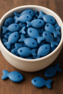 a white bowl filled with blue fish shaped crackers on a wooden table