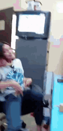 a man wearing a shirt that says ' a ' on it sits in front of a television