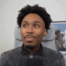a man with curly hair and a beard is sitting in a chair with a microphone in front of him