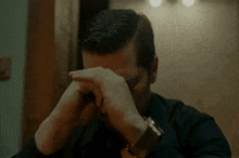 a man with a watch on his wrist covering his face with his hands