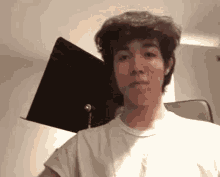 a young man wearing a white t-shirt is making a funny face .