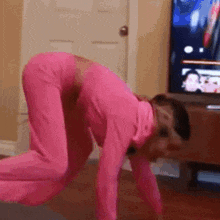 a woman in a pink bodysuit is doing push ups on a yoga mat in a living room .
