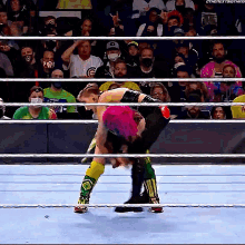 two wrestlers are wrestling in a ring with a crowd in the background .