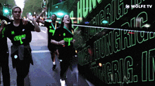 a group of people walking down a street with a wolfe tv logo behind them