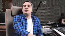 a man wearing glasses and a plaid shirt is sitting in front of a piano