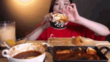 a woman in a red shirt is eating food from a bowl with chopsticks