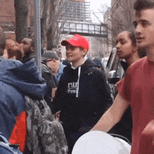 a boy wearing a red hat and a hoodie that says i 'm full of pesticides stands in a crowd of people