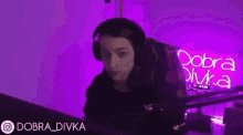 a woman wearing headphones gives a thumbs up in front of a purple sign that says dobra